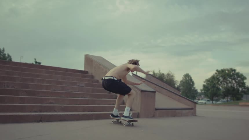 Male skateboarder jumps a flight of steps outdoors on a cloudy summer day