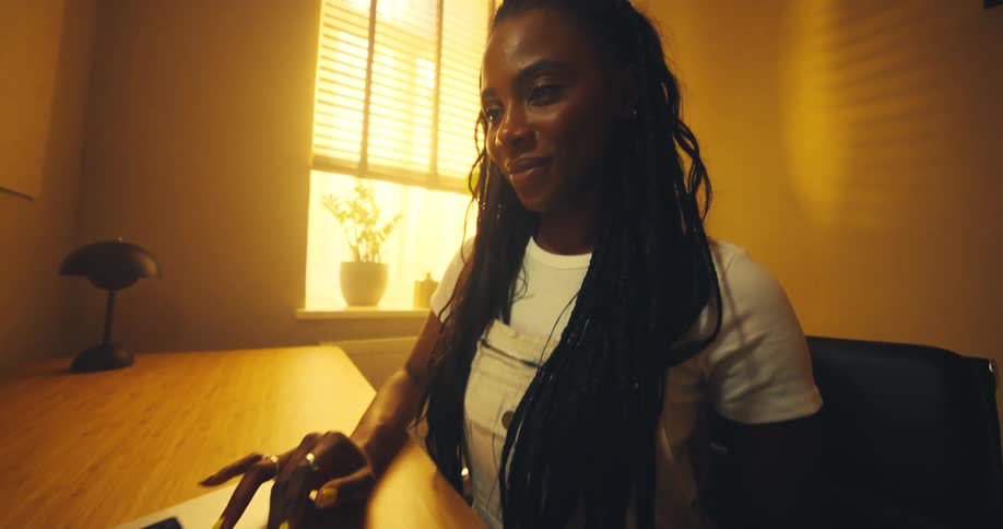 The face of a young woman with a subtle smile as she uses a laptop on a wooden table