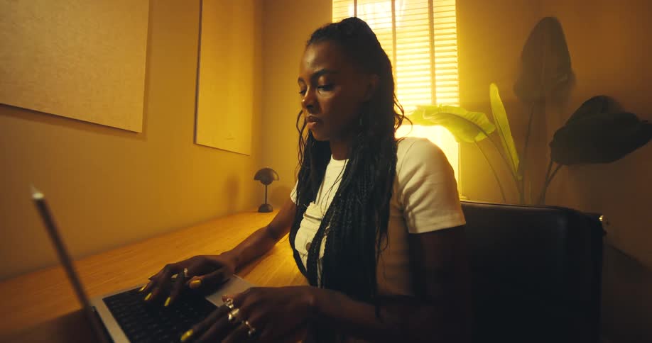 A woman types on a laptop at a wooden desk in a warm amber lit office