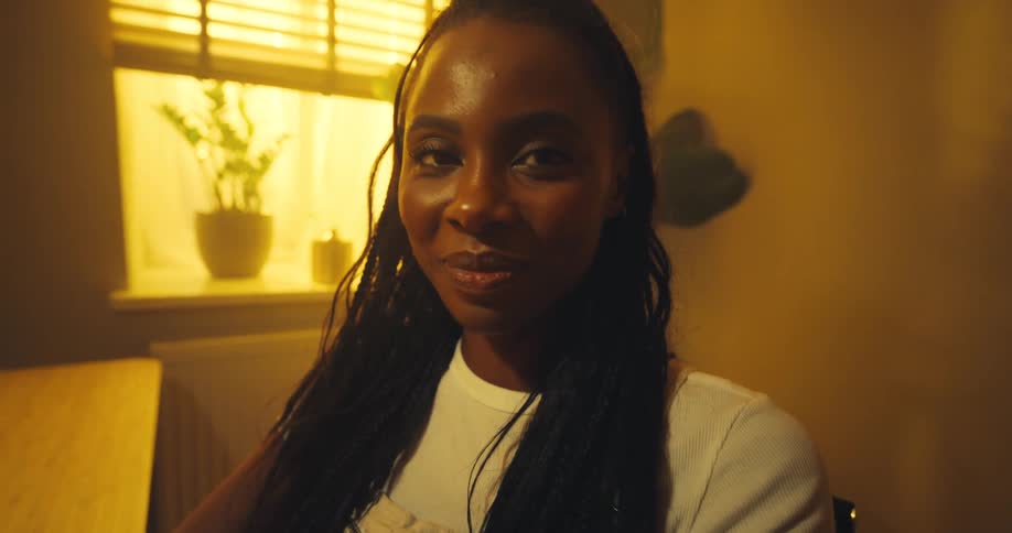 A closeup of hands typing on a laptop cuts to a young woman looking up and smiling in a warm sunlit room