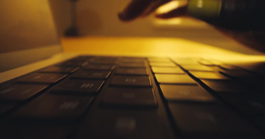 A closeup shot shows hands typing quickly on a laptop keyboard lit by a warm glow