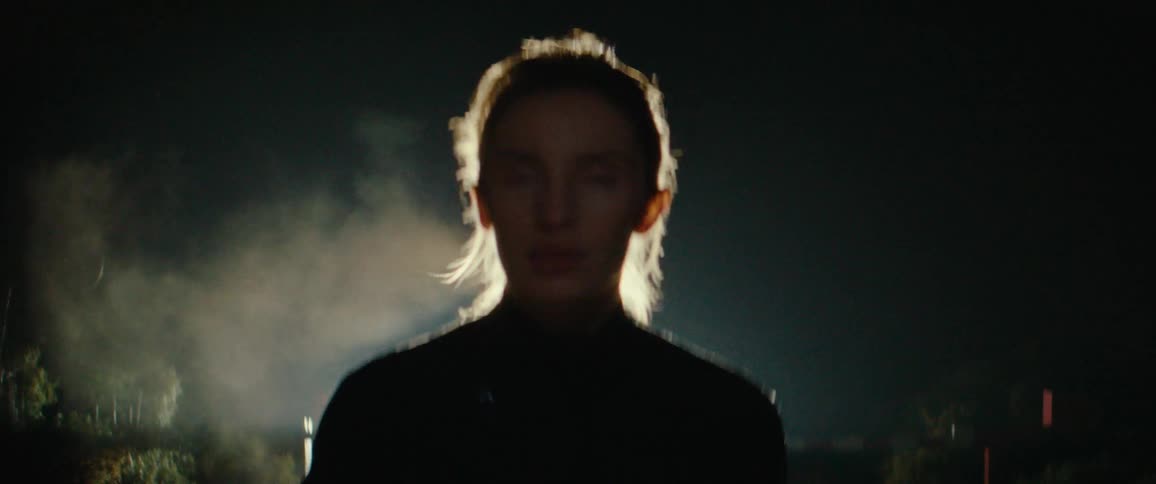 A woman staring straight ahead while running outdoors in the dark with a light illuminating her back
