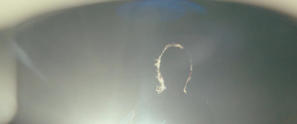 A woman is silhouetted against a bright backlight with dramatic lens flares as the camera pulls back