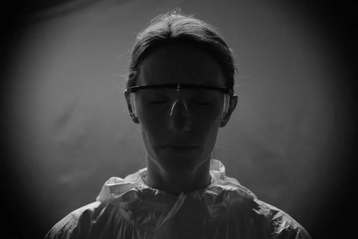 Woman wearing protective coverall and safety goggles under spotlight in dark setting