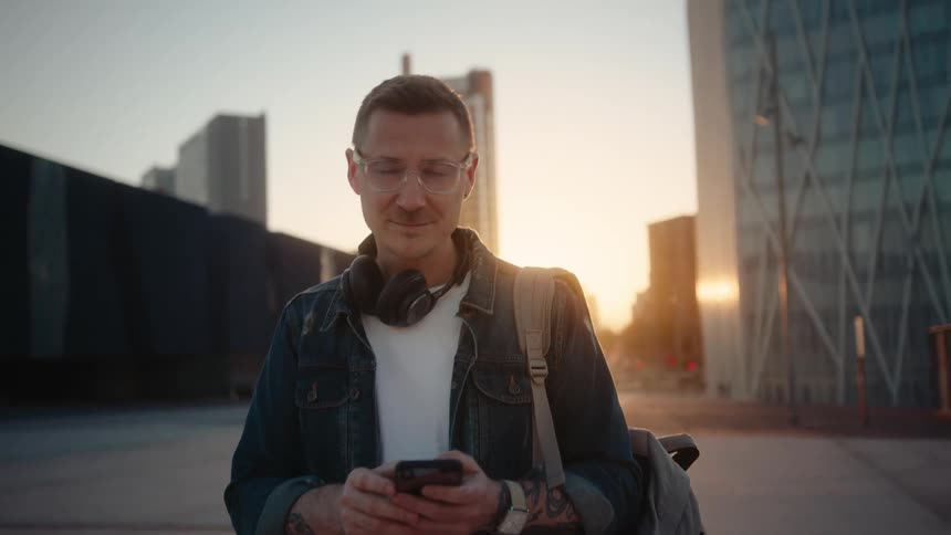 The man is smiling while using his phone and walking