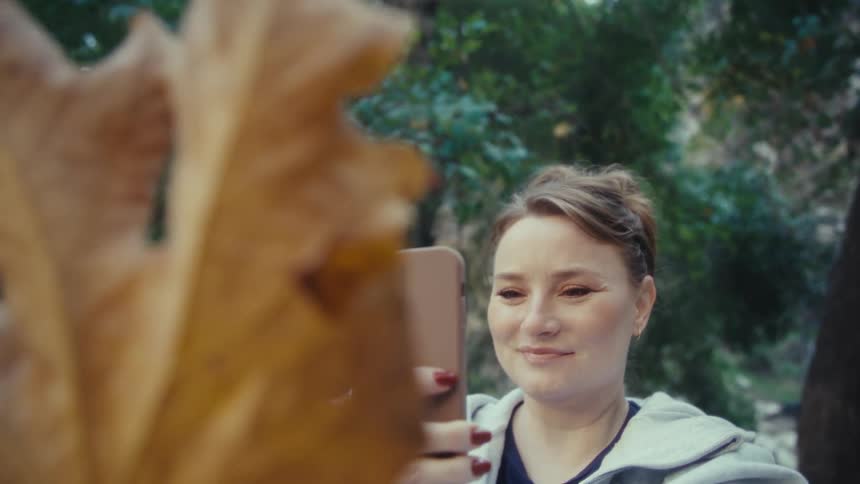 Woman holds her camera as she takes a picture of a leaf