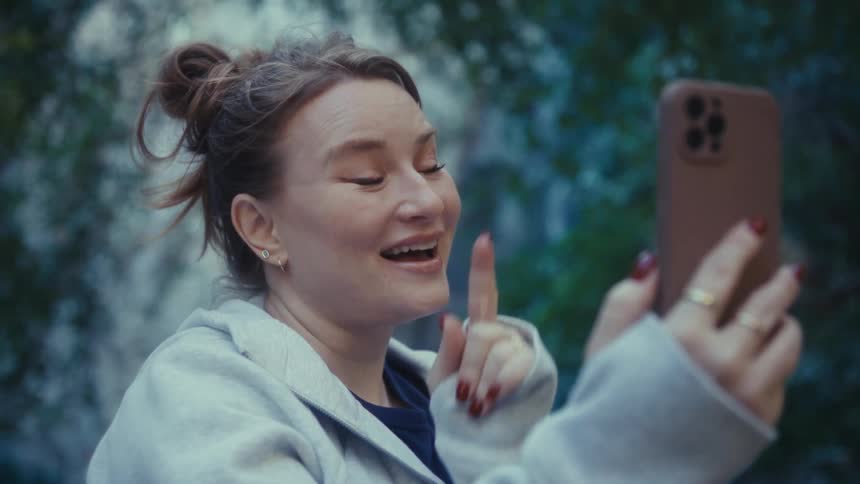 Woman holds her phone and smiles as she points her finger in conversation