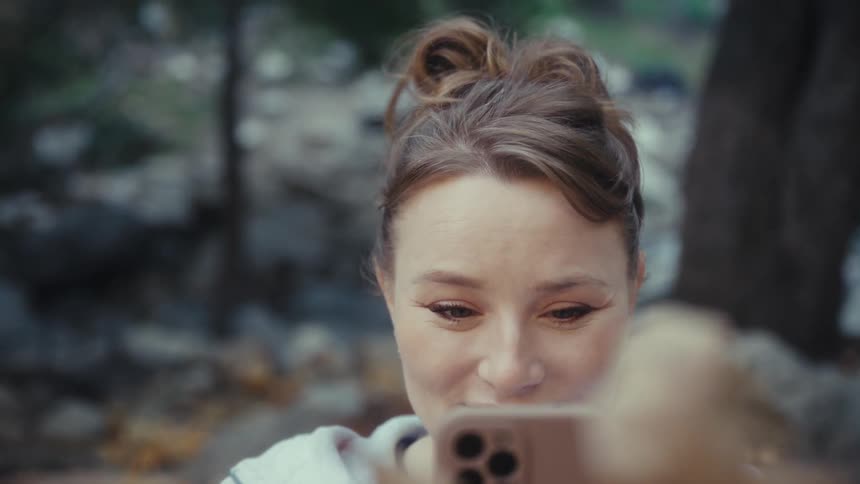 Person with tiedup hair using phone to photograph autumn leaves in natural setting with rocks and trees