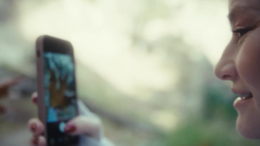 Brown autumn leaf being photographed with smartphone on forest floor covered in fallen leaves