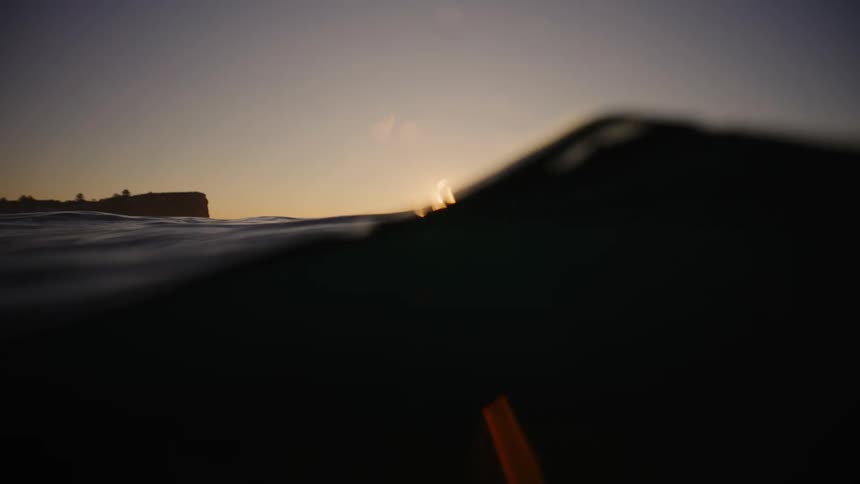 Setting sun reflected on gentle ocean waves with cliff to the left and tranquil atmosphere
