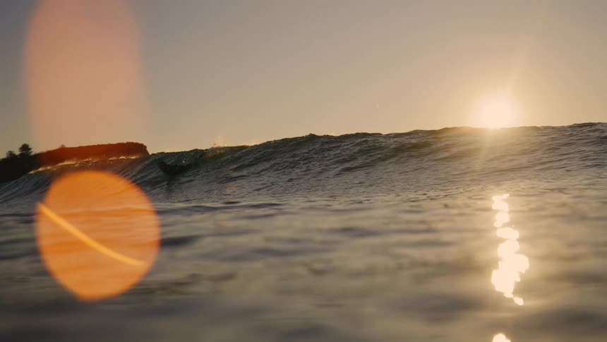 A few surfers are surfing at dusk in a body of water with choppy waves a nearby by mountain area in the distance
