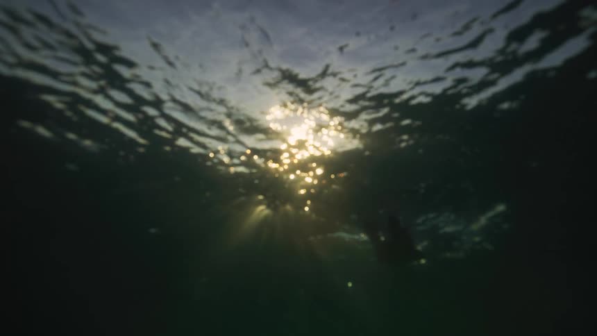 View from underwater as the sun shines through the ripples and waves as it sets