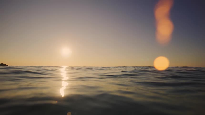 Two individuals in the sea with golden sunset reflection