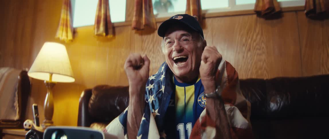 Man smiles and claps excitedly wrapped in the united states flag in front of a projector