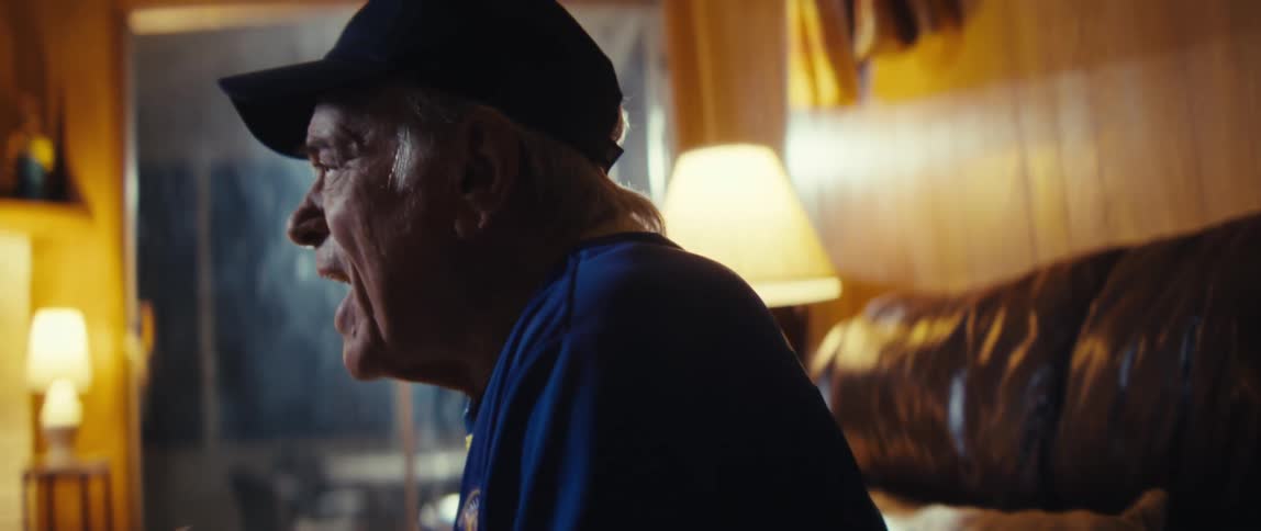 Elderly man wearing baseball cap and football jersey cheering and clapping in a living room indoors during night time