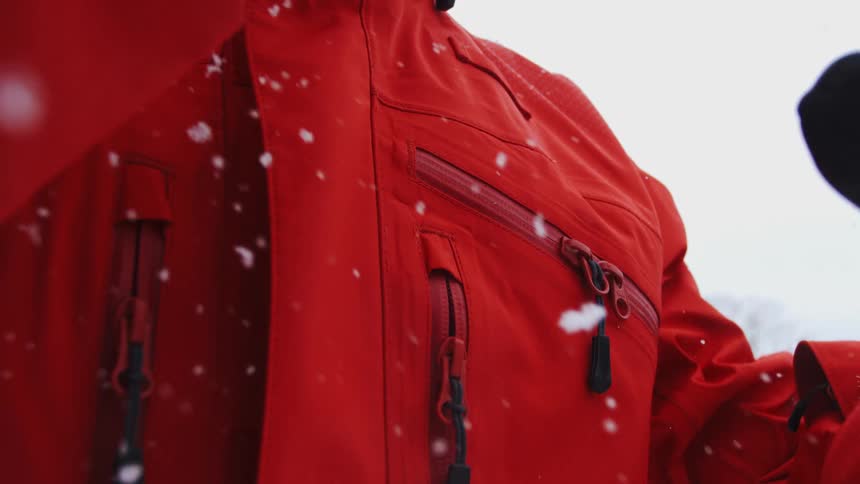 Snow falling on red jacket in outdoor setting with white sky and branches in the background