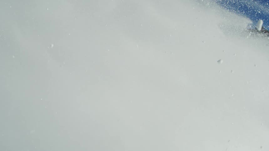 An avalanche rushes down a hill at midday with snow cascading downhill in a powerful flow