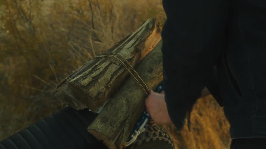 Bundle of firewood tied with rope on a motorcycle seat in dry terrain