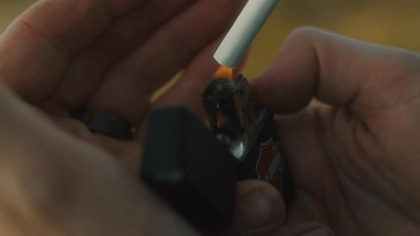 A closeup captures hands lighting a cigarette with a harleydavidson lighter
