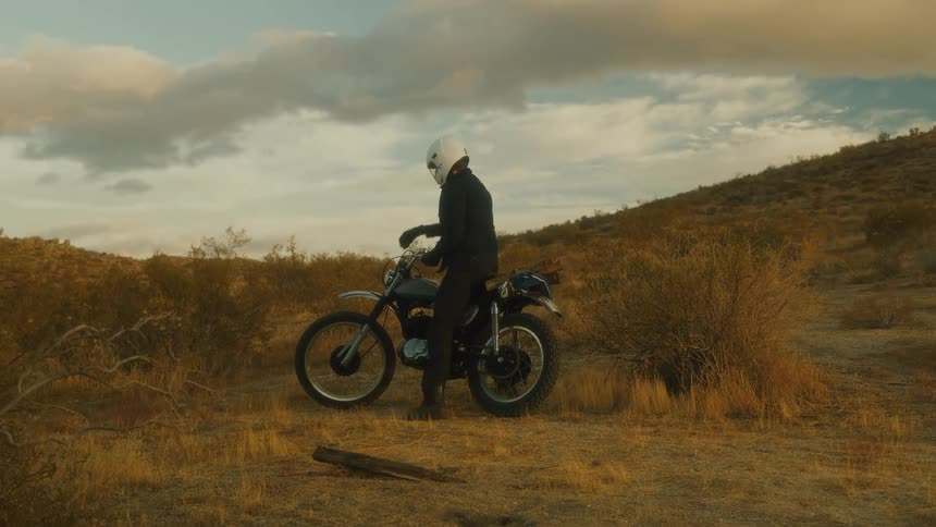 Man dismounts the motorcycle in the dry open landscape