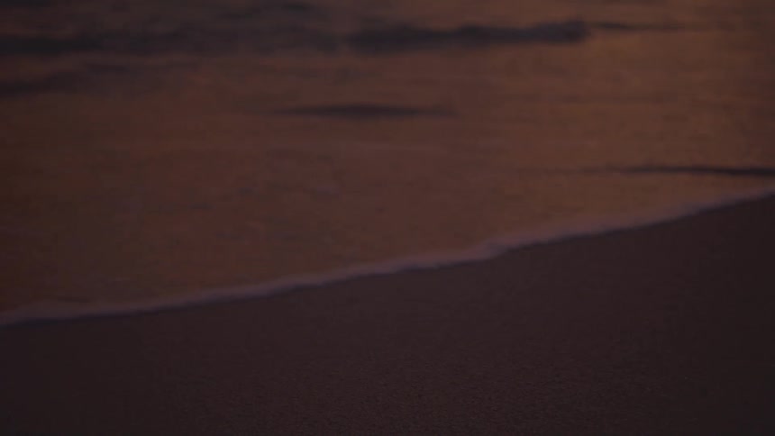 Gentle waves reach the sand under the pink evening light