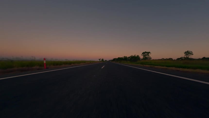 Paved road stretches between fields beneath orangetoned sky