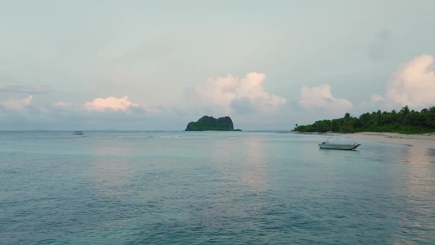 Boat anchored near beach with forest behind and rocky island under pastel sky