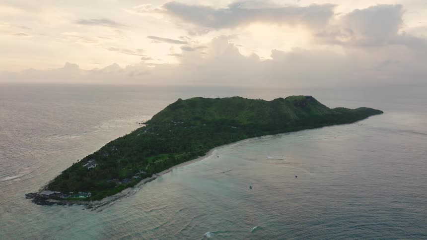 Small boats sail off the coast of a vegetated island