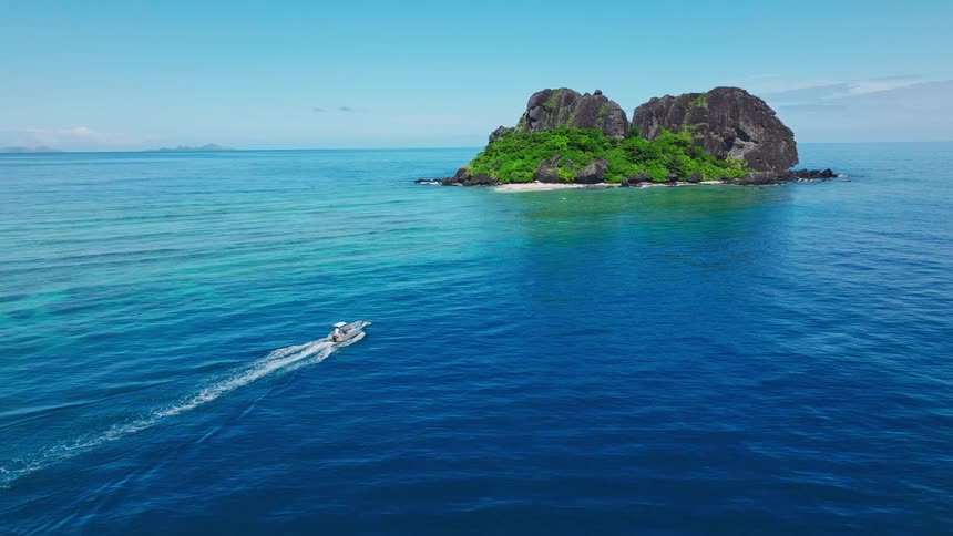 Island with green cliffs and pale beach welcomes boat in deep blue waters under clear sky