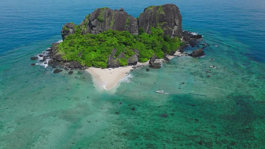 A boat glides across the ocean at midday heading toward a mountainous island rising in the distance