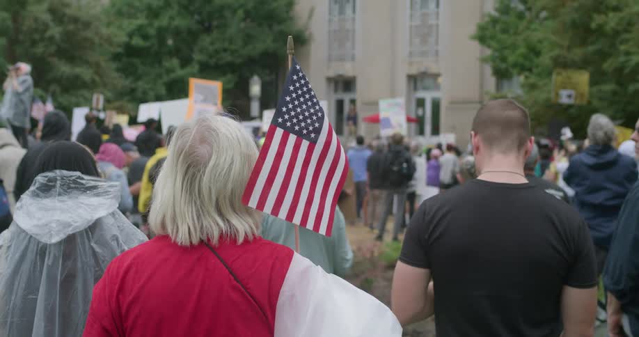 People holding placards in protest and waving american flag while standing outside a public building