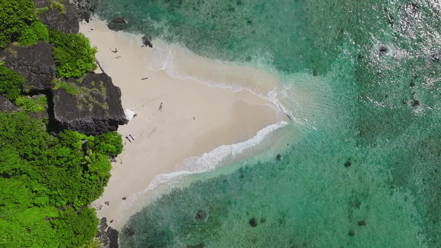Tropical beach with turquoise waters laps sandy shore between cliffs and lush greenery