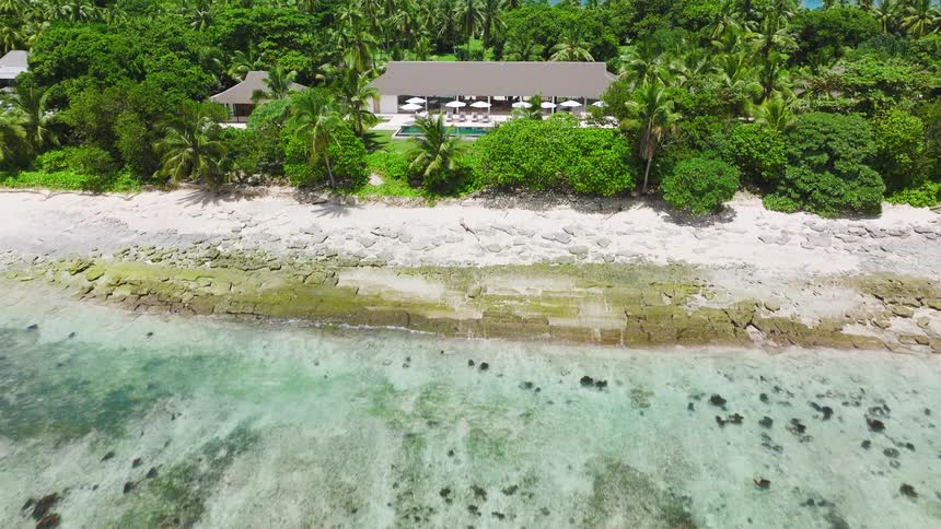A resort sits on a tropical island surrounded by the ocean under the bright midday sun