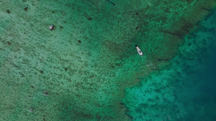 Boat sails near reef in turquoise waters fading into deep ocean blue