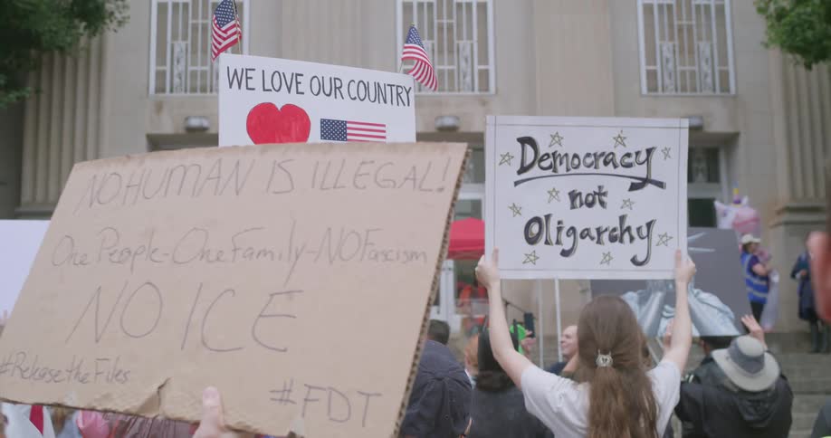 Crowd of people holding signs of a political nature in front of a building in an urban area outdoors during day time