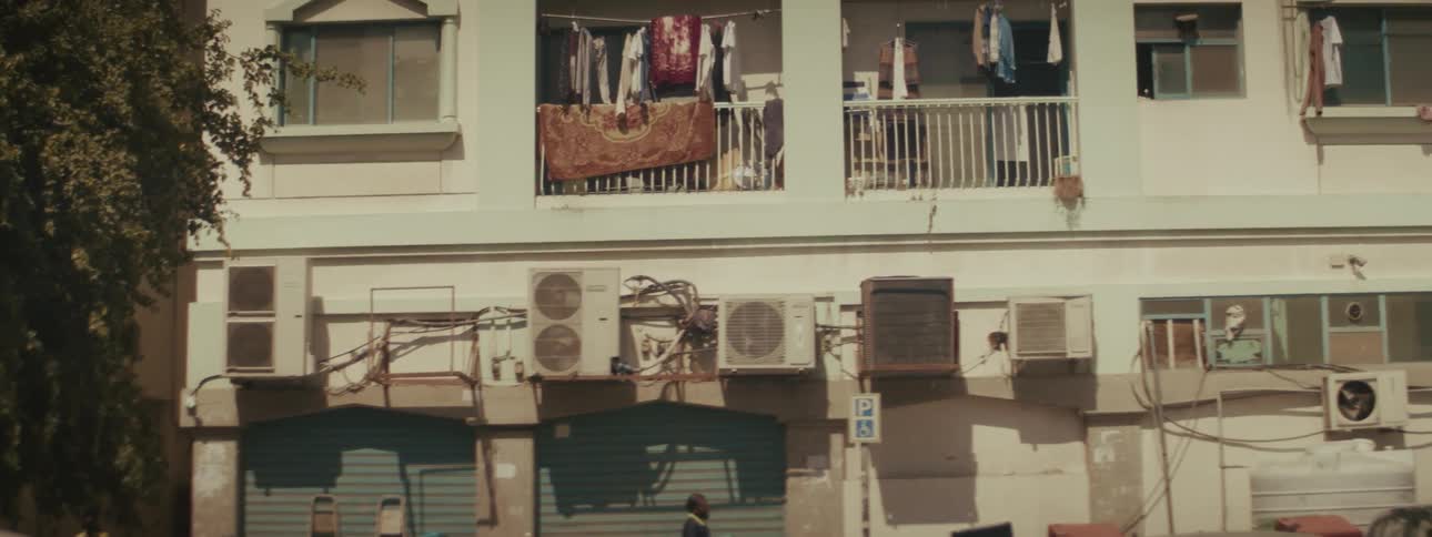 Urban building facade shows clothes hanging on balconies air conditioners and shuttered storefronts at street level