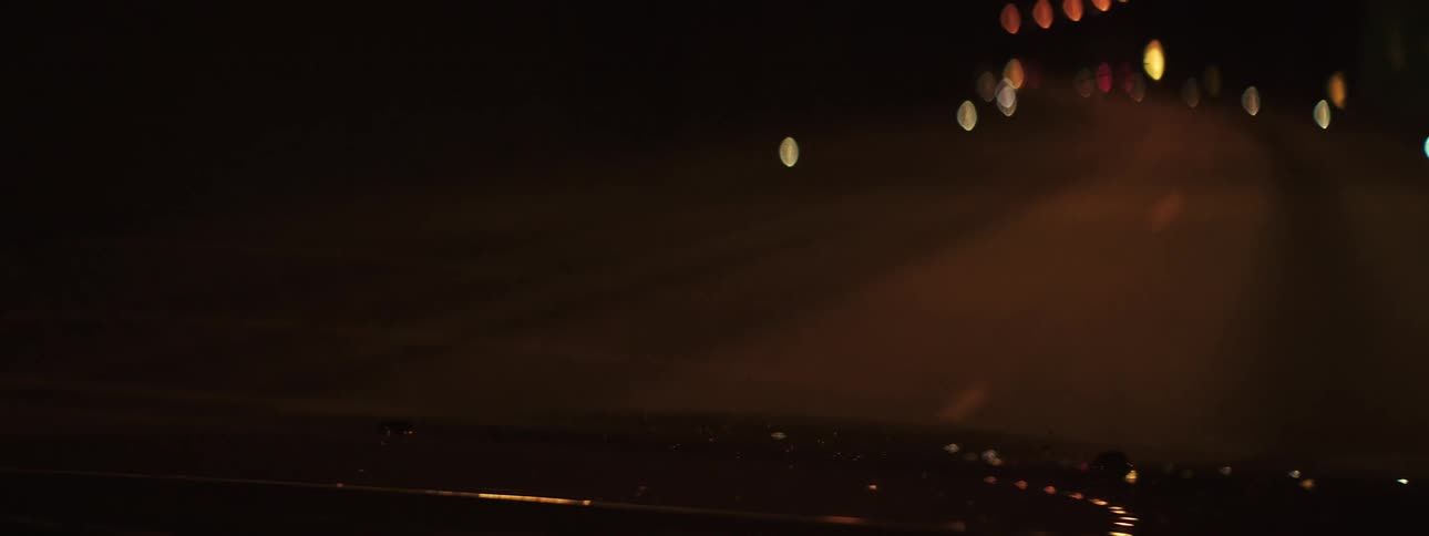 Nighttime view through windshield shows road lit by streetlights and headlights under dark sky