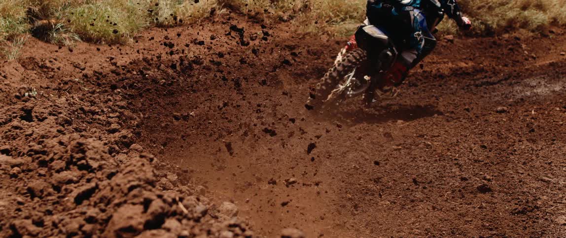 Motocross rider leans into turn on dirt track kicking up dust in intense maneuver