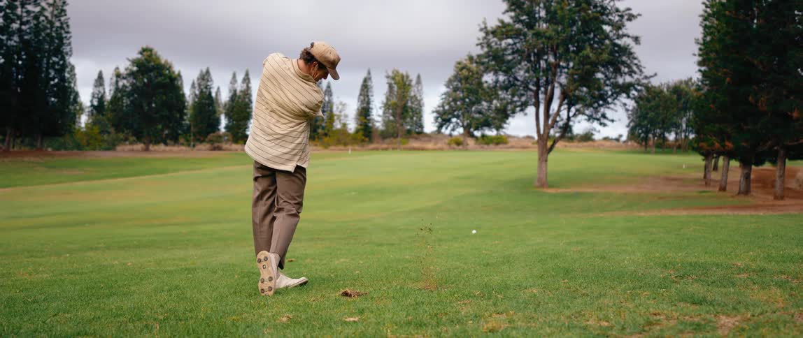 Golfer stands with his club in the air then swings and hits golf ball