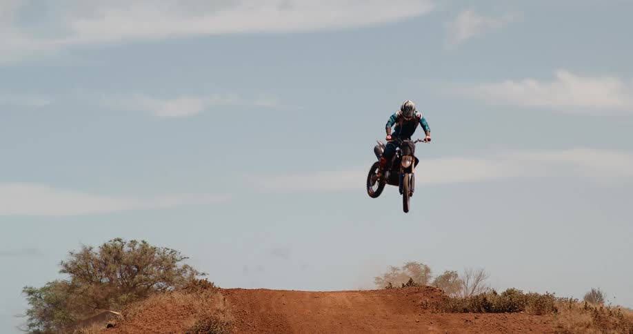 Motorcyclist flies over dirt track after jump in open setting with partly cloudy sky