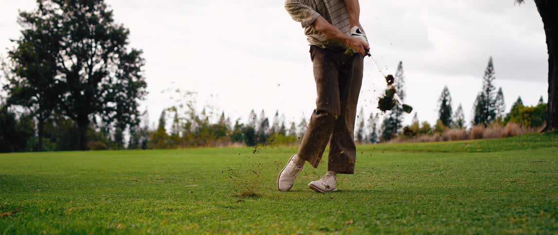 A man hits the golf ball with the golf club along with a little sand at midday