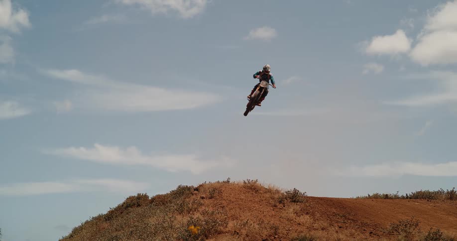 Motorcyclist performing a jump on a dirt track under a sunny sky