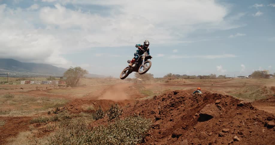 A dirt bike rider performs a mid air jump on a dusty track under a cloudy sky