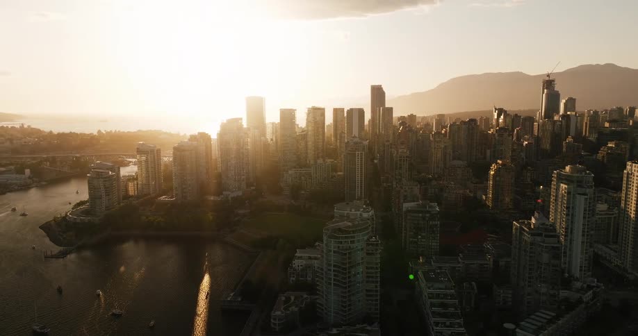 Golden sun lights coastal city with skyscrapers boats on water and mountains in the background
