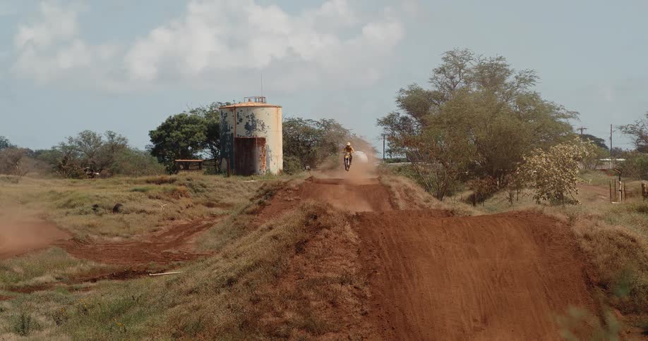 Two motocross riders performing stunts on a dirt track at midday
