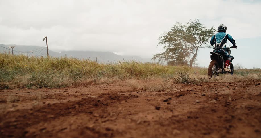 Motorcyclist speeds along dirt trail with red boots and rear wheel in focus