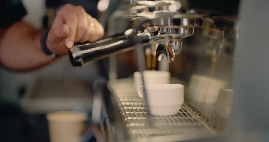 A barista pulls a shot on a professional espresso machine with two white cups waiting below