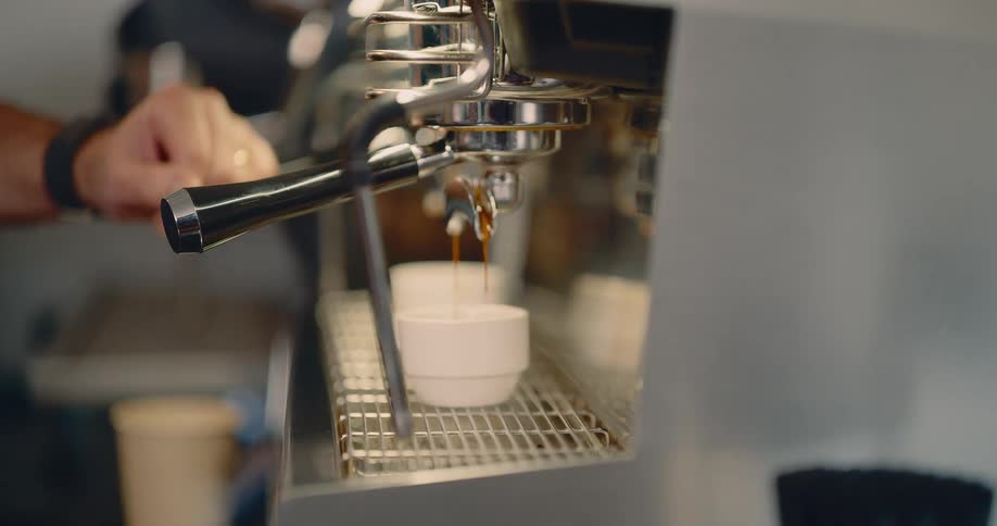 Dark coffee flows from espresso machine spout into white cup during brewing process