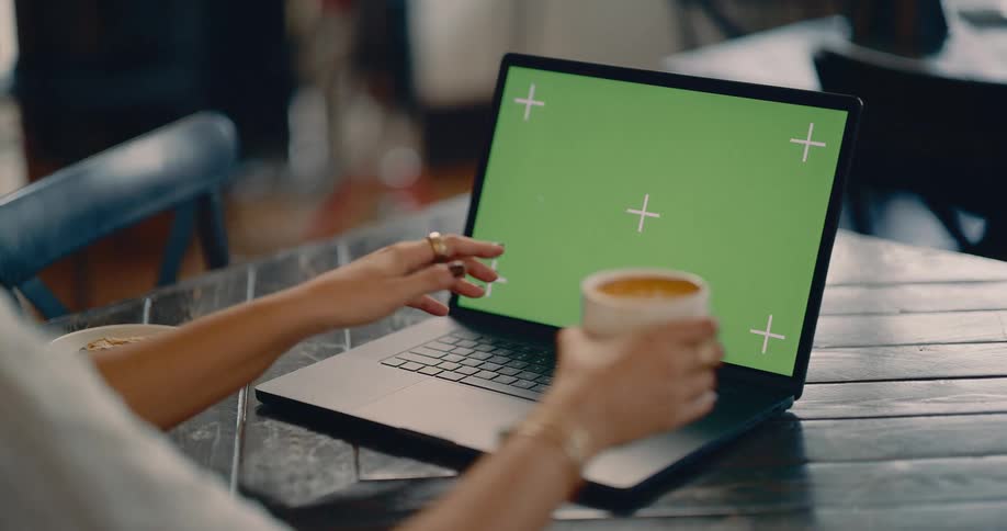 A female is sitting at a table in a room indoors drinking from a cup and typing on a laptop