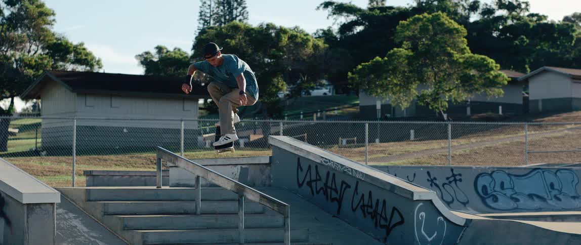 Skateboarder slides on handrail amid ramps and graffiti at outdoor urban skatepark